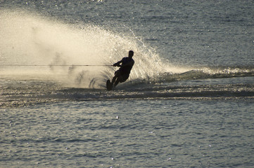 Silhouette wakeboarder creating large spray on lake during summe