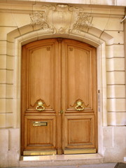 Porte cochère marron, poignées dorées, façade de pierre