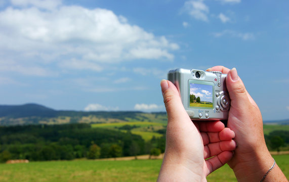 Hands with digital camera and shot of summer countryside