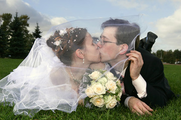 bride and groom laying on the grass kissing