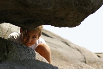 A boy peeking between large rocks
