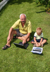 The grandfather with grandson sit on a green grass
