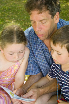 father with daughter and son reading in park