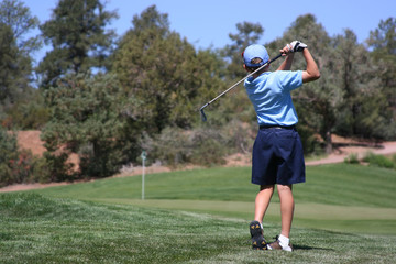 Young male hitting ball on green, focus on golfer