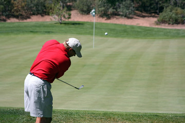 Man chipping ball onto green, focus on golfer