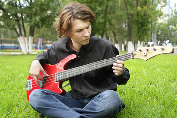 teenage boy playing the bass guitar on the lawn