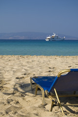 Lonely deck chair with a view over a blue lagoon and a yacht