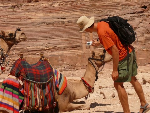 Male tourist taking picture of lying camel, Petra, Jordan