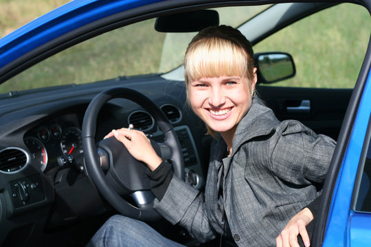young blond woman in a blue car/ She is smiling happy