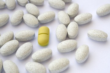 Fototapeta na wymiar Yellow pill among gray tablets