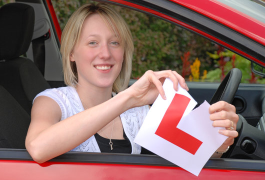 Smiling woman in car holding ripped L plate - passed test