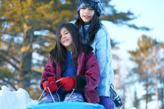 Two children having fun sledding down hill in winter