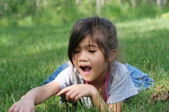 GIrl lying on grass excited about  interesting object in grass
