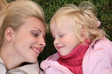 Happy smiling mother and daughter lie on green grass