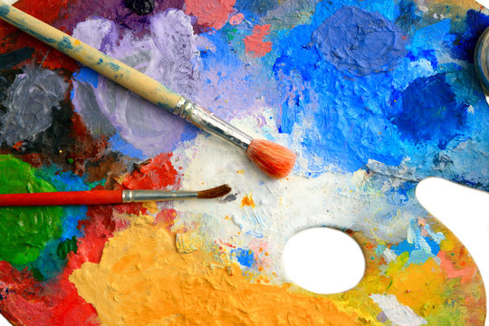 Two Brushes lay on an art palette in bright paints