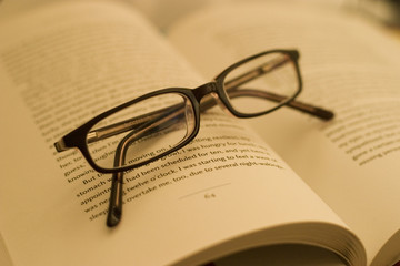 A pair of reading glasses and a novel under the lamp