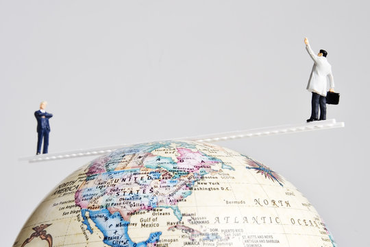Business figures placed on a ladder balancing on an earth globe.
