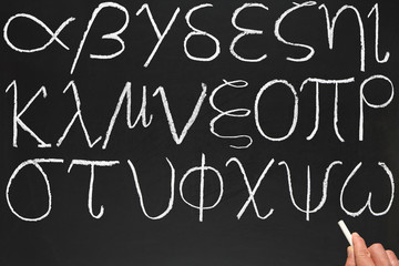 A teacher writing the Greek alphabet on a blackboard.