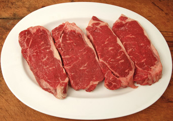 raw New York strip steaks on a platter