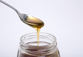 spoon full of honey above glass pot