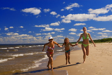  Mother and two daughters running on a beach near the water