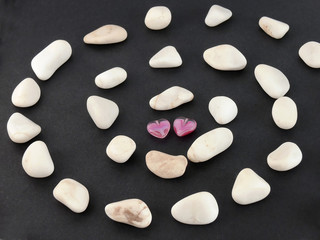 Two beaded hearts and stone spiral on black background