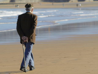 Anciano con bastón paseando por la playa