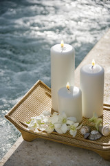 Lit pillar candles on tray with white orchids beside pool.
