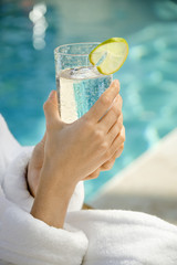 Woman's hands holding beverage glass with lime slice.