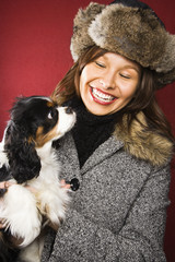 Woman wearing fur hat holding dog in arms and smiling.