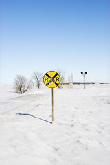 Railroad crossing sign in snow covered rural landscape.