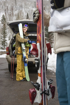 Couple standing with ski equipment by open vehicle smiling.