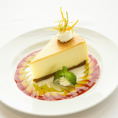 Slice of cheesecake garnished with sauce and mint sprig.