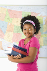 Girl standing in front of USA map holding books smiling.