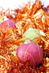 Three pink and yellow Christmas baubles with orange tinsel 