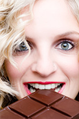 Blondes Mädchen mit aufgerissenen Augen beißt in Schokolade