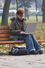 Obraz premium Redhead girl working on a latop in an autumn park.