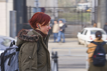 Obraz premium Redhead girl listening to music while walking in a city. 