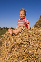 Naklejka na ściany i meble laughing barefooted baby boy sit on a hayrick