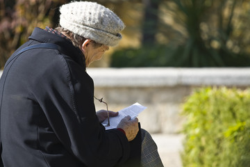 Old woman reading a letter in the park.
