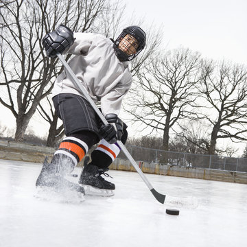 Boy in ice hockey uniform skating on ice rink moving puck.