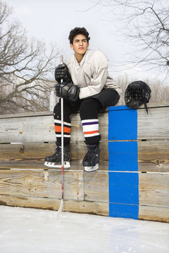 Boy in ice hockey uniform holding hockey stick.