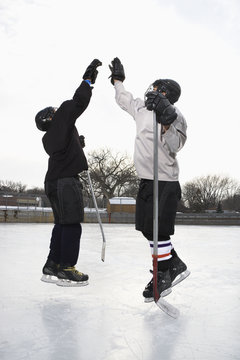 Two boys in ice hockey uniforms giving eachother high five.