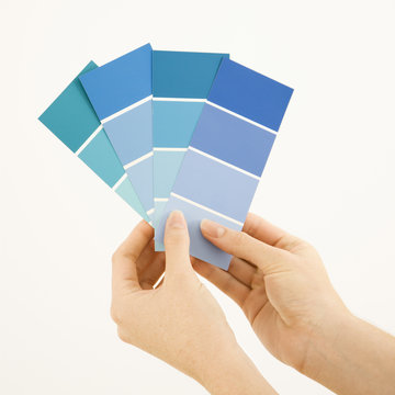 Caucasian female hands holding paint color swatches.