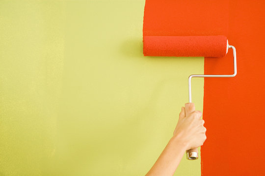 Caucasian Female Hand Painting Red Over A Green Wall.