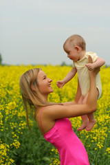 Fototapeta premium Happy mother with her child in yellow flowers field
