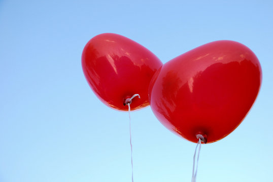 Ein Paar roter Herzluftballons vor blauem Himmel