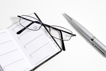 Glasses, pen and notebook on white background.