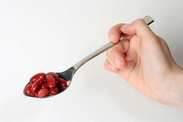 Red raw haricot on stainless serving spoon, on white