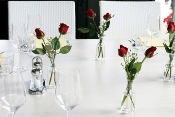 Elegant table setting with vases of red roses and white linen.